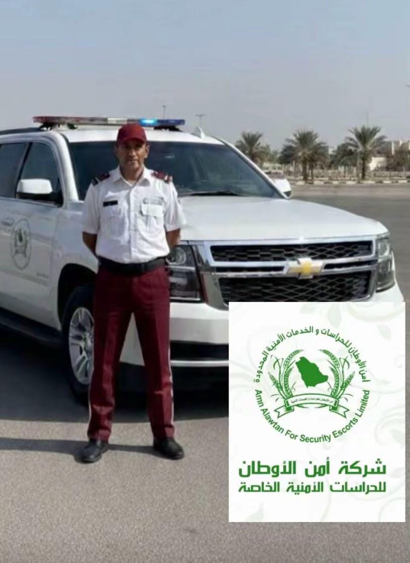 حارس أمن من شركة أمن الأوطان بالزي الرسمي يقف أمام سيارة دورية أمنية